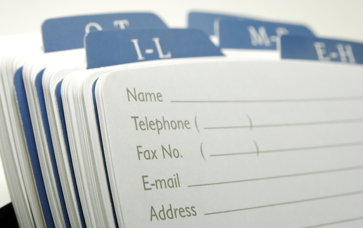 A close-up of a paper address book with alphabetical tabs. The visible page has blank fields for name, telephone, fax number, email, and address. Tabs for "I-L" and neighboring letters are visible.